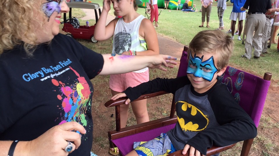 A woman is painting a boy's face at an outdoor event.