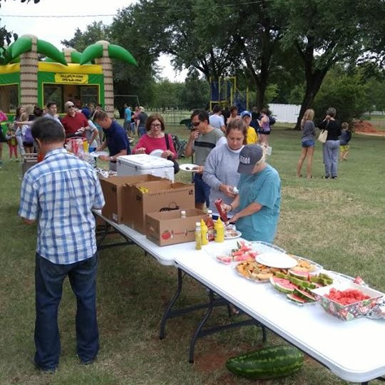 A group of people standing around a table in a park.