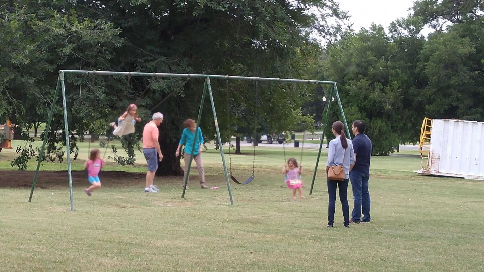 A group of people playing on a swing set in a park.