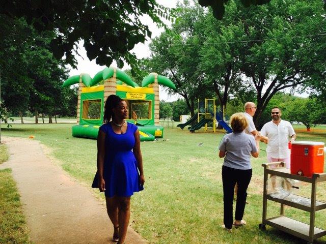 A woman in a blue dress standing next to a bounce house in a park.