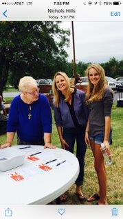 Three women standing in front of a table with a sign.