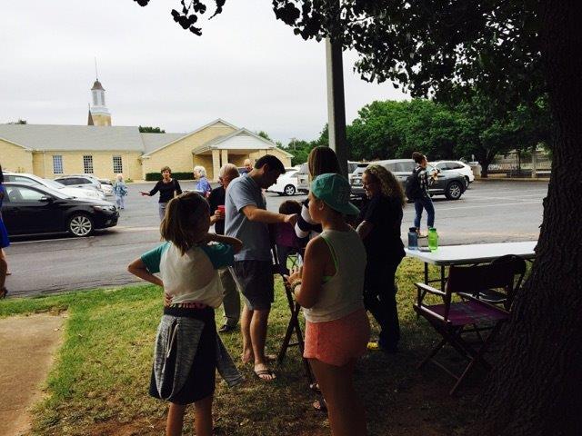 A group of people standing under a tree in front of a church.