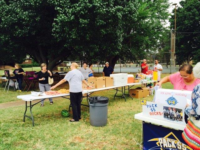 A group of people standing around tables in a park.