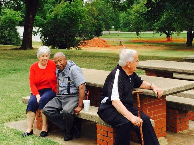 Three people sitting on a bench in a park.