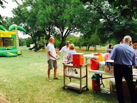 A group of people standing around a table in a park.
