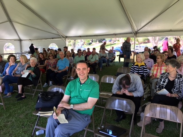 A large group of people sitting in chairs under a tent.