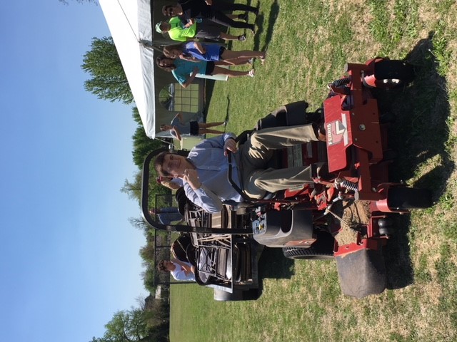 A man standing next to a red lawn mower on a grassy field.