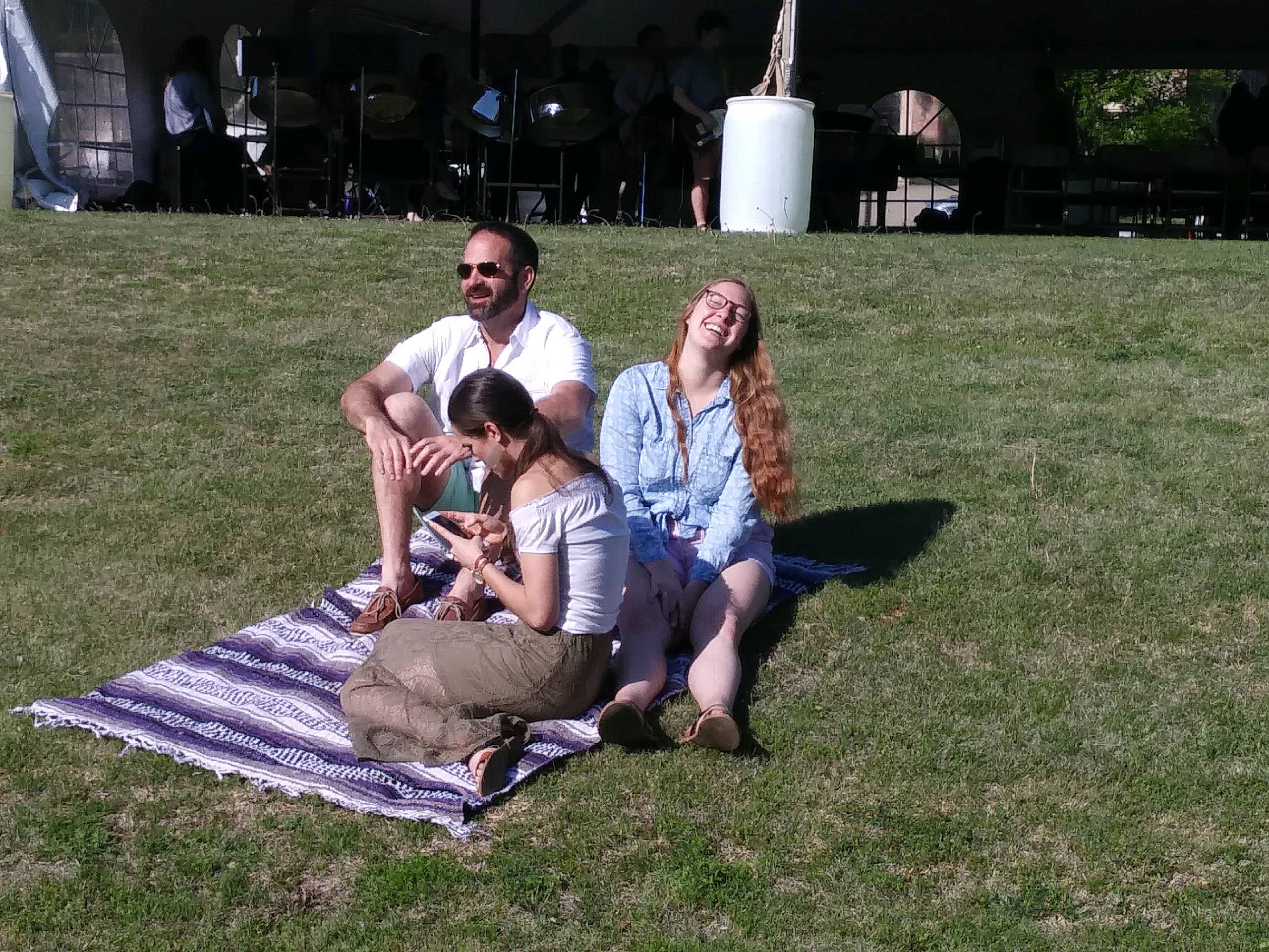 Three people sitting on a blanket under a tent.
