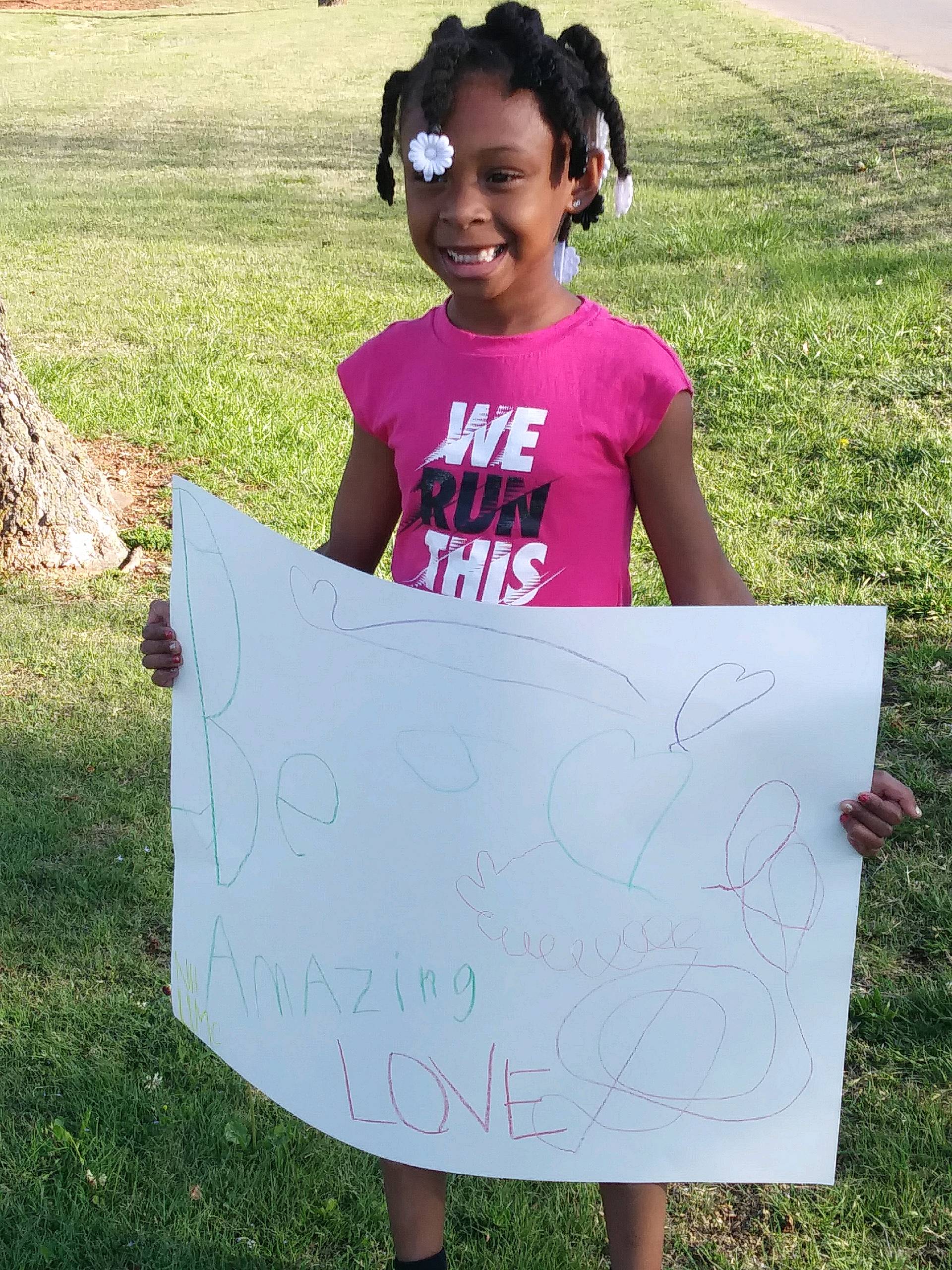A little girl holding up a sign that says we are amazing love.