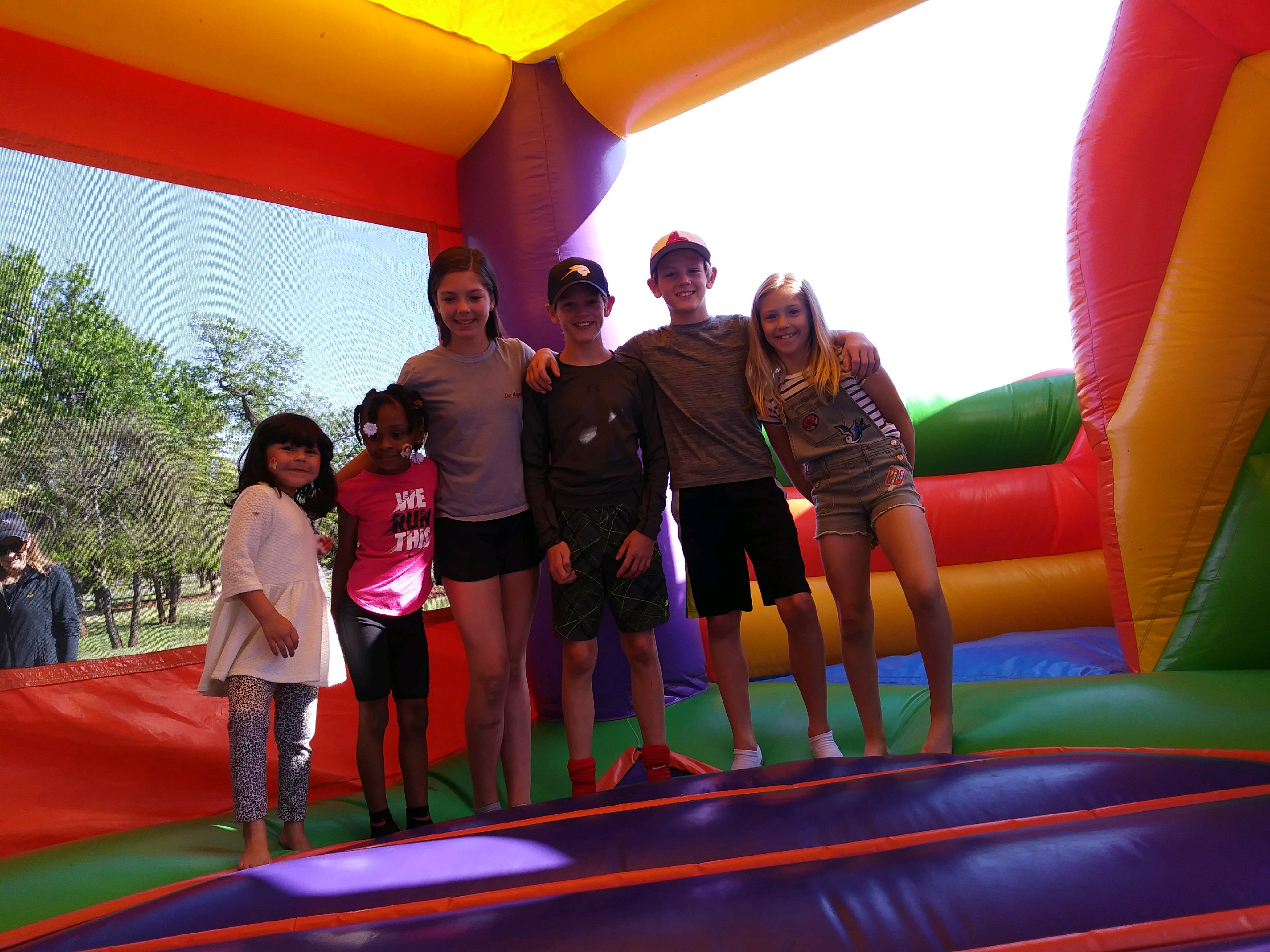 A group of kids posing in front of a colorful bouncy castle.