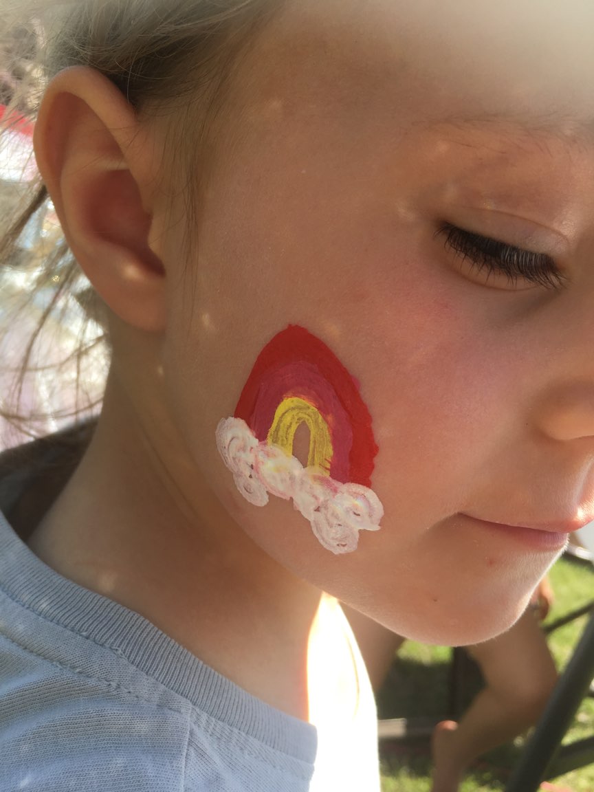 A little girl with a rainbow painted on her face.