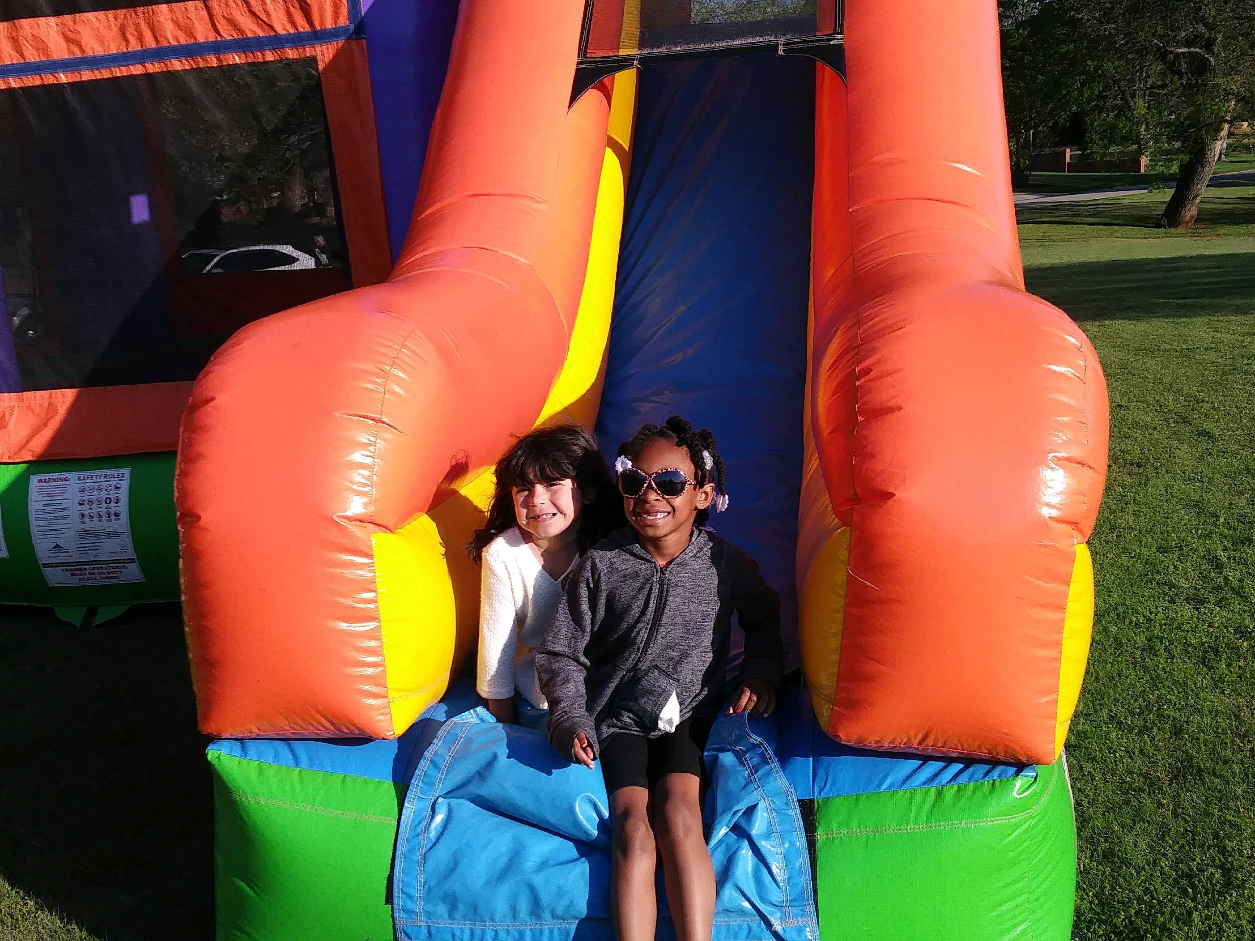 Two children sitting on the slide of a bounce house.