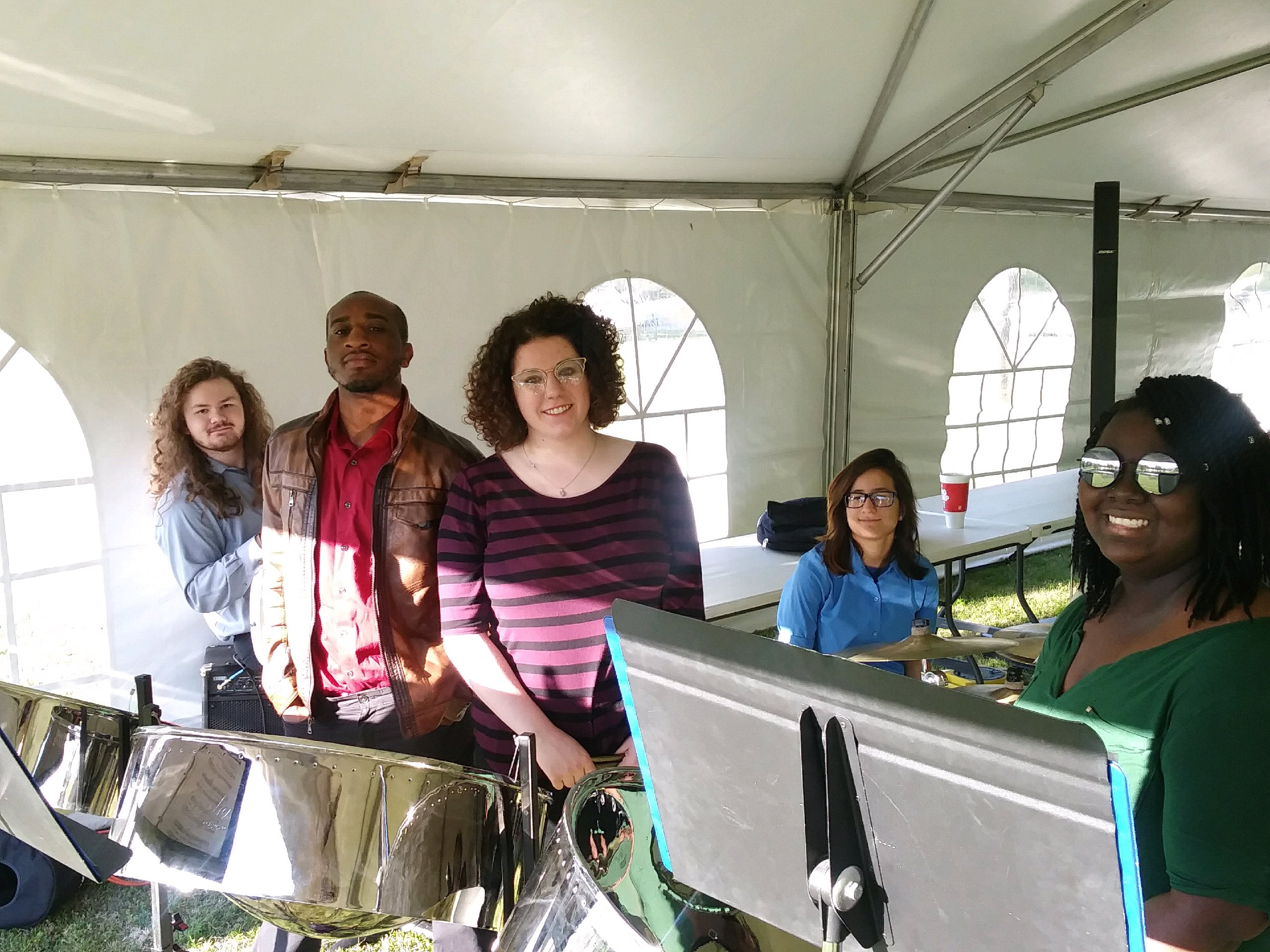 A group of people standing in front of a tent with steel drums.