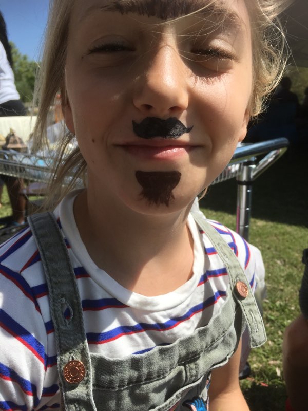 A little girl with a mustache on her face.