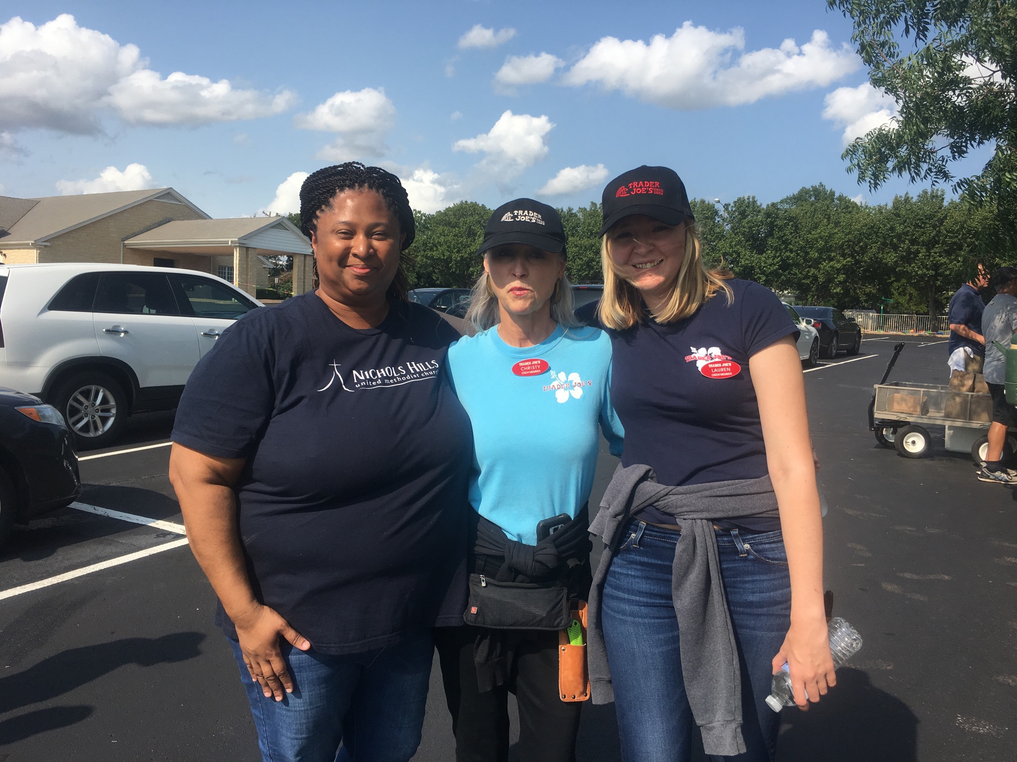 Three women posing for a photo in a parking lot.