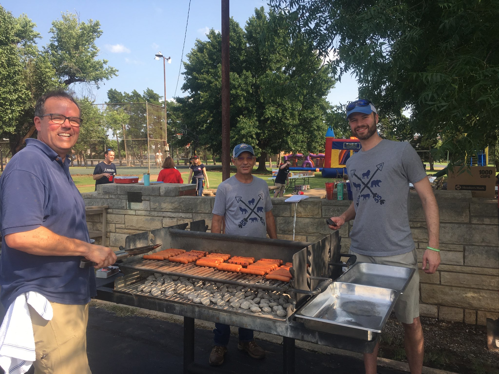 A group of men standing next to a bbq grill.