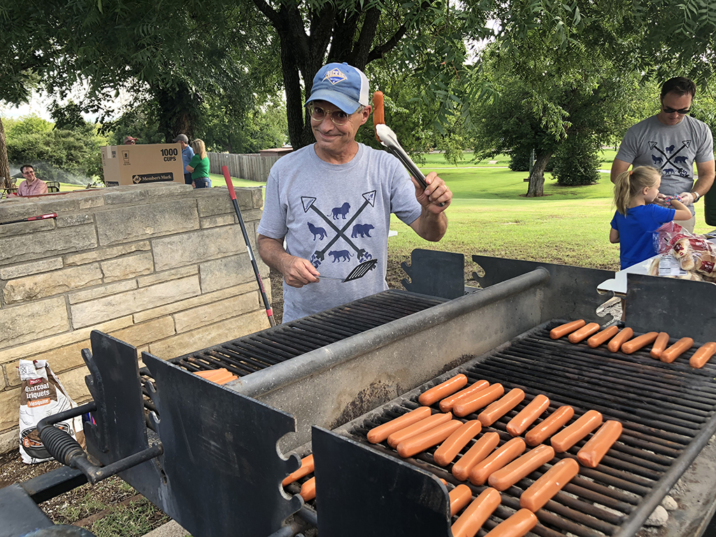 A group of people grilling hot dogs on a grill.