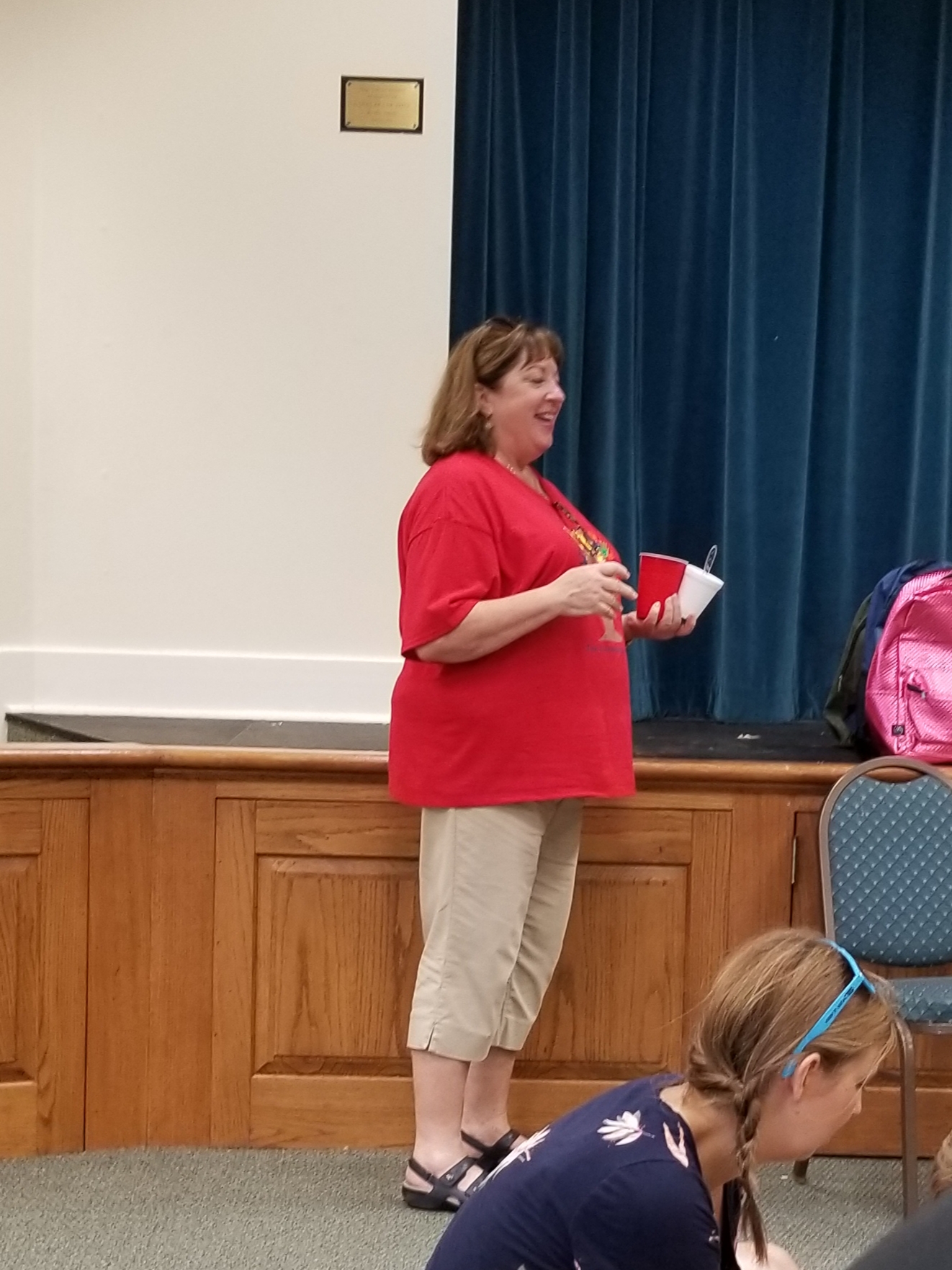 A woman in a red shirt standing in front of a group of people.