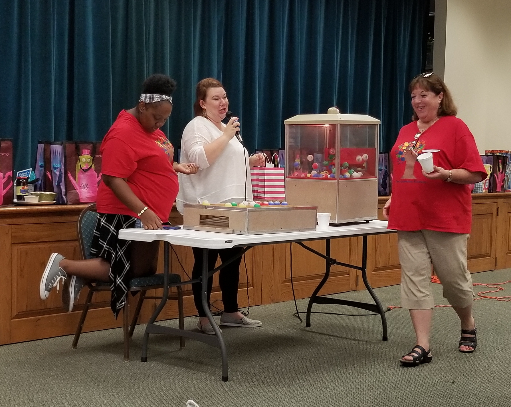 Three women standing around a table with a candy machine.