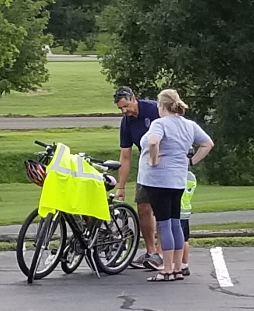 A group of people standing next to a bike in a parking lot.