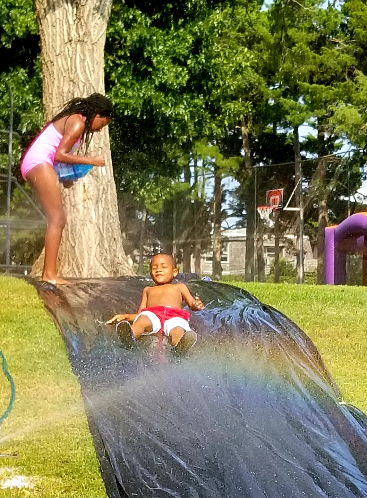 A girl and a boy slide down a water slide in a park.