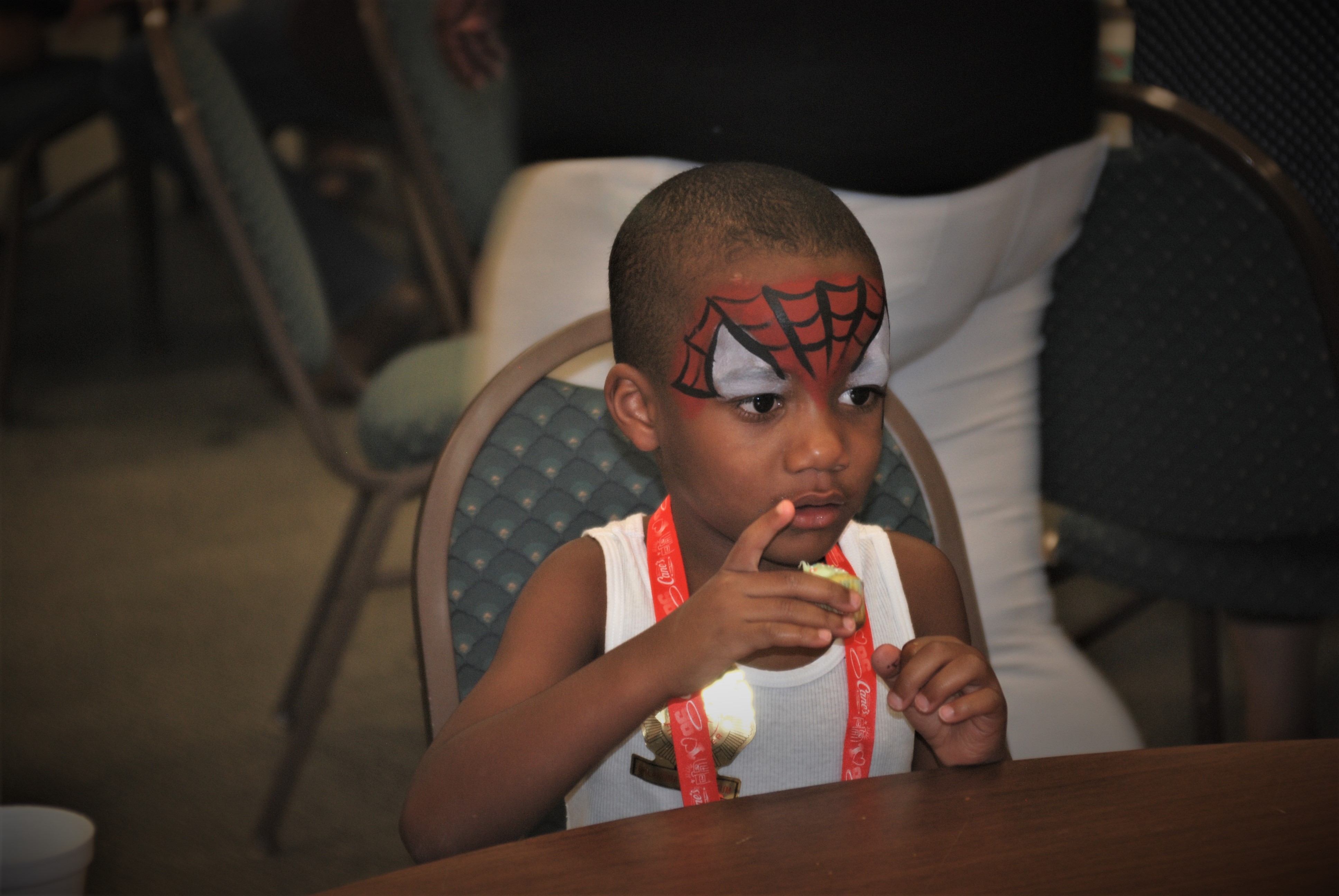 A young boy sitting at a table with a spider - man face paint.