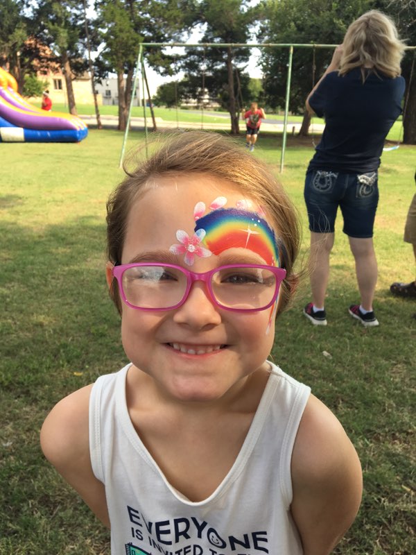 A little girl with glasses and a rainbow painted on her face.
