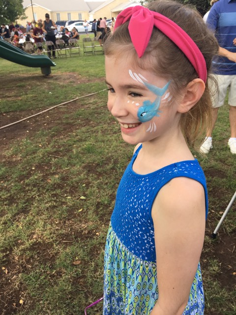 A little girl wearing a blue dress and blue face paint.