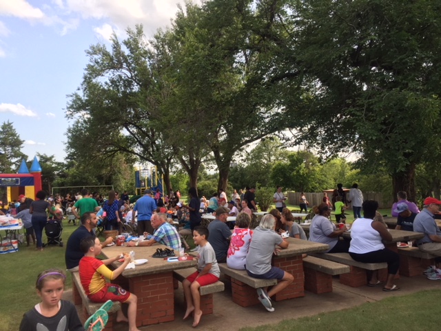 A group of people sitting at tables in a park.