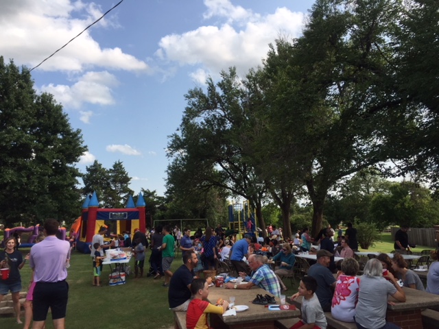 A crowd of people at a picnic table in a park.