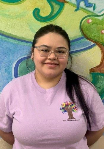 A woman in a purple shirt standing in front of a mural.